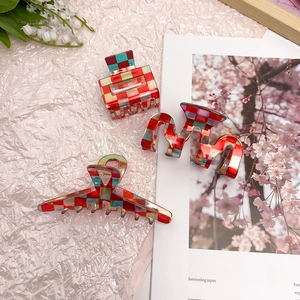 Detailed view of red and green checkerboard acetate hair claws on a decorative background