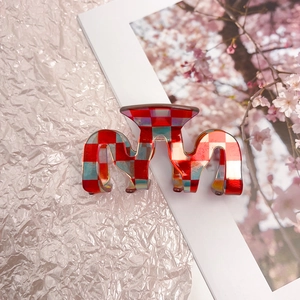 Detail of M-shaped acetate hair claw featuring a vibrant red and blue checkerboard pattern