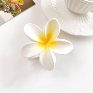 Detail of matte white plumeria flower hair claw clip with yellow center on white desk