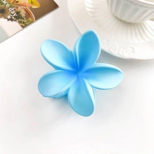 Detail showing matte light blue frangipani flower hair claw clip on a white background