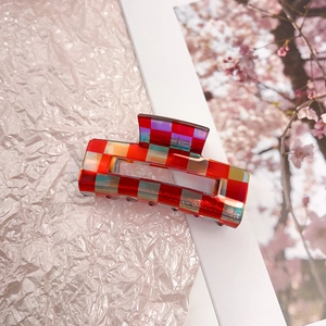 Detail of red checkered acetate hair claw clip with laser finish on a white frame