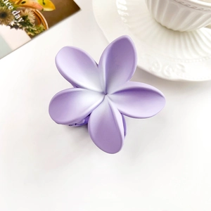 Detail view of a matte purple flower hair claw clip with gradient petals on a white desk