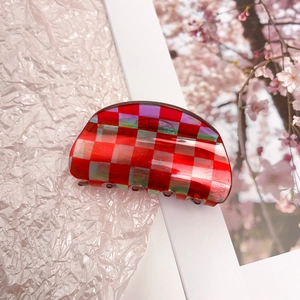 Macro shot of red checkered acetate hair claw clip on white frame with cherry blossoms