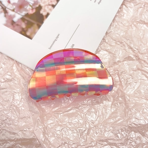 Detailed close-up of iridescent checkered hair claw clip on pink fabric background
