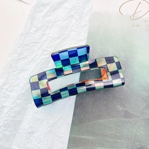 Detail showing checkered hair claw clip with blue and cream squares on a textured background