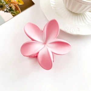 Detailed macro view of a matte pink plumeria hair claw clip on a white table