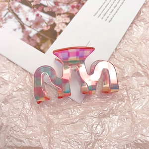 Detailed view of the wavy iridescent checkerboard claw clip on a pink paper background