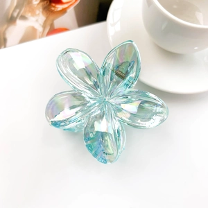 Detail shot of light blue iridescent flower hair claw clip on a minimalist white saucer
