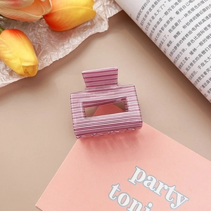 Détail de la pince à cheveux à rayures roses et blanches sur un fond esthétique
