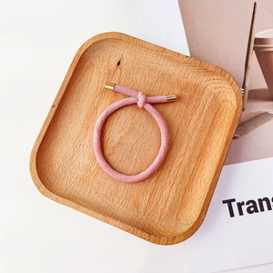 Vue détaillée de l'élastique à cheveux rose avec texture sergée et embouts dorés