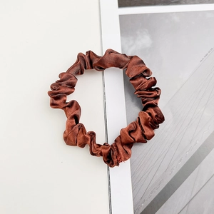 Vue détaillée d'un chouchou en satin marron foncé avec des plis doux sur magazine