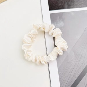 Détail rapproché d'un chouchou en satin blanc crème avec texture soyeuse et pli élastique