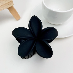 Détail d'une pince à cheveux fleur noir mat sur un fond blanc minimaliste