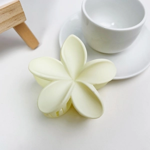 Détail d'une pince à cheveux frangipanier jaune crème mat sur un bureau minimaliste