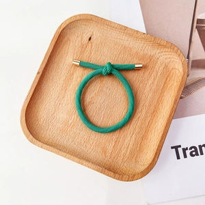 Détail d'un élastique à cheveux vert torsadé avec boucle en métal doré sur plateau en bois