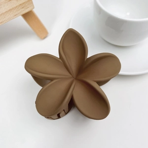 Détail d'une pince à cheveux fleur marron mat sur un bureau blanc au style épuré