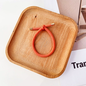 Détail d'un élastique tressé orange vif avec des embouts métalliques dorés sur un plateau