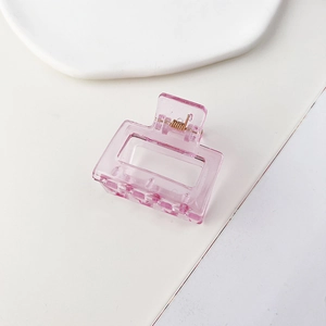 Dettaglio di pinza per capelli quadrata rosa trasparente con molla dorata su sfondo bianco