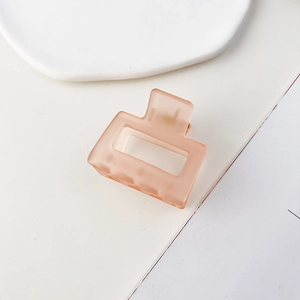 Dettaglio di un fermaglio per capelli quadrato color pesca opaco su vassoio minimalista