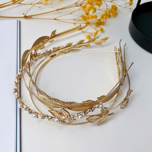 Dettagli di cerchietti dorati con foglie di metallo, perle e strass su bianco