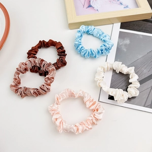 Five pack of assorted satin silk scrunchies in pastel tones on a minimalist white desk