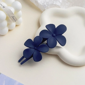 Detail of matte navy blue double flower hair clip on a white wave tray with a candle