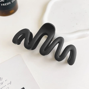 Macro detail of a black matte wave hair claw clip on a minimalist aesthetic background