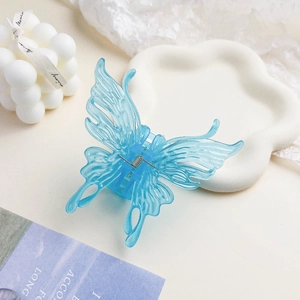 Détail d'une pince à cheveux papillon bleu clair translucide sur un plateau nuage blanc