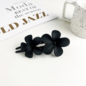 Close-up of matte black double floral hair clip on a minimalist lifestyle desk background