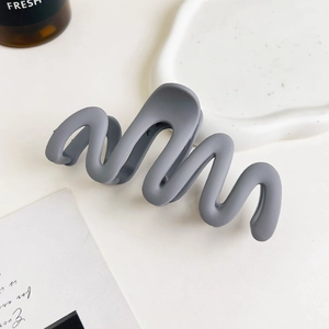 Detail view of a matte grey wavy hair claw clip styled on a minimalist tray background