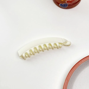 Dettaglio di un fermaglio a banana bianco crema opaco con denti curvi su sfondo bianco