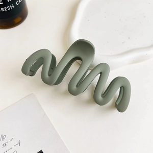 Close-up of wavy matte dark green shark clip on a minimalist decorative white tray