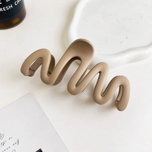 Close-up of matte wave hair claw clip in milk tea brown on a decorative white ceramic tray