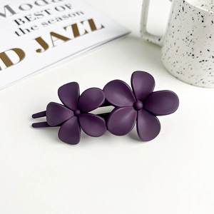 Detailed close-up of dark purple matte double flower hair clip on a white table surface