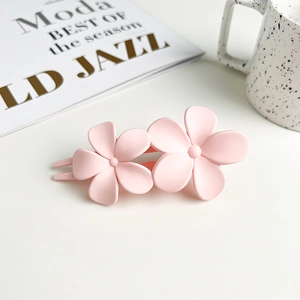 Close-up of pink matte double flower hair clip next to a ceramic cup on a white table