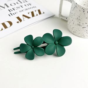 Detail of dark green double flower hair clip with matte finish on white desktop