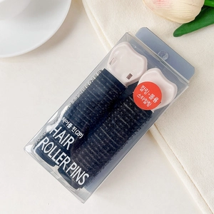 Detail of two black hair rollers with pink clips in a clear PVC display box on a desk