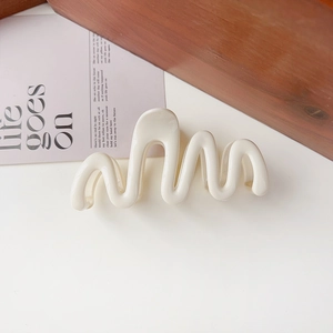 Detailed view of a creamy white wave-shaped hair claw clip on a minimalist wooden setting