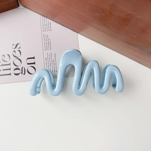 Detail of light blue wavy hair claw clip on white surface with a wooden block