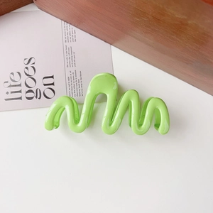 Detail of light green wavy claw clip on white surface with modern minimalist design