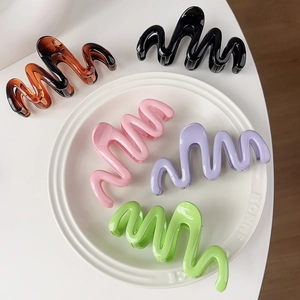 Set of wavy cream-colored hair claws in five vibrant colors displayed on a white plate