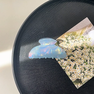 Detail of a large pearlescent blue acrylic hair claw clip on a black textured tray