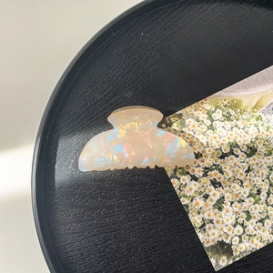 Detail view of iridescent beige acetate hair claw clip on black wood tray with daisy card
