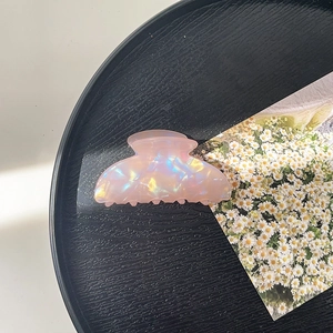 Detail of pink iridescent resin hair claw clip with shell texture on black tray