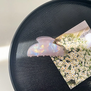 Detail of an iridescent pink acrylic hair claw clip with a pearlescent finish and shimmery glow