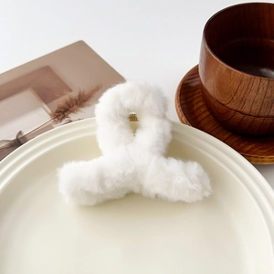 Détail de la pince à cheveux croisée en peluche blanche avec ressort doré sur une assiette