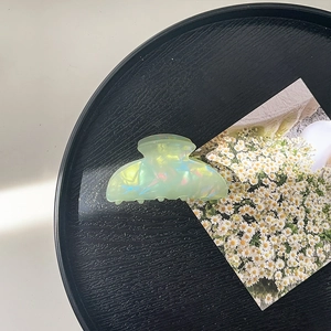 Detail view of large light green pearlescent acrylic shark hair claw clip with colorful sheen