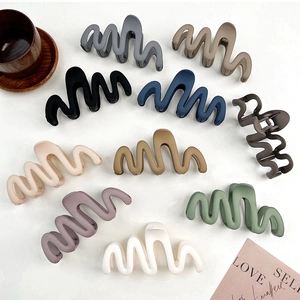 Flat lay showing wave-shaped matte hair claws in various Morandi colors on a grey surface