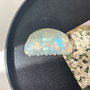 Detail view of pearlescent acrylic hair claw clip with colorful shell texture on black tray