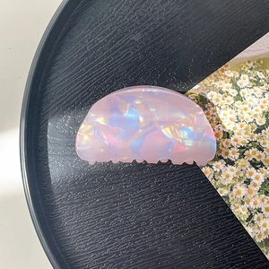 Detailed top view of a pearlescent shell-shaped hair claw clip on a minimalist black tray